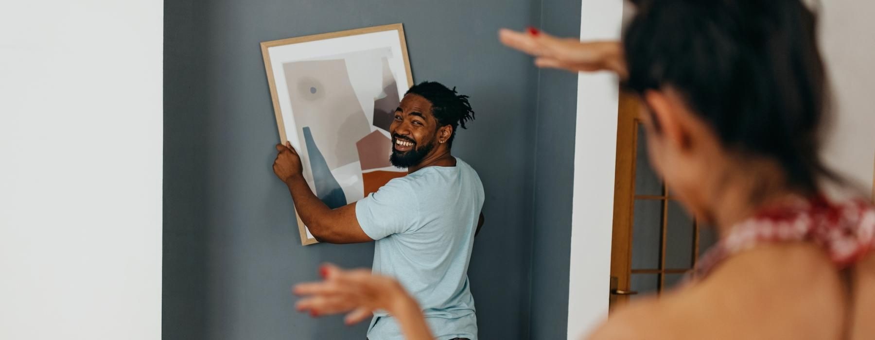 a man and woman in a room hanging a picture