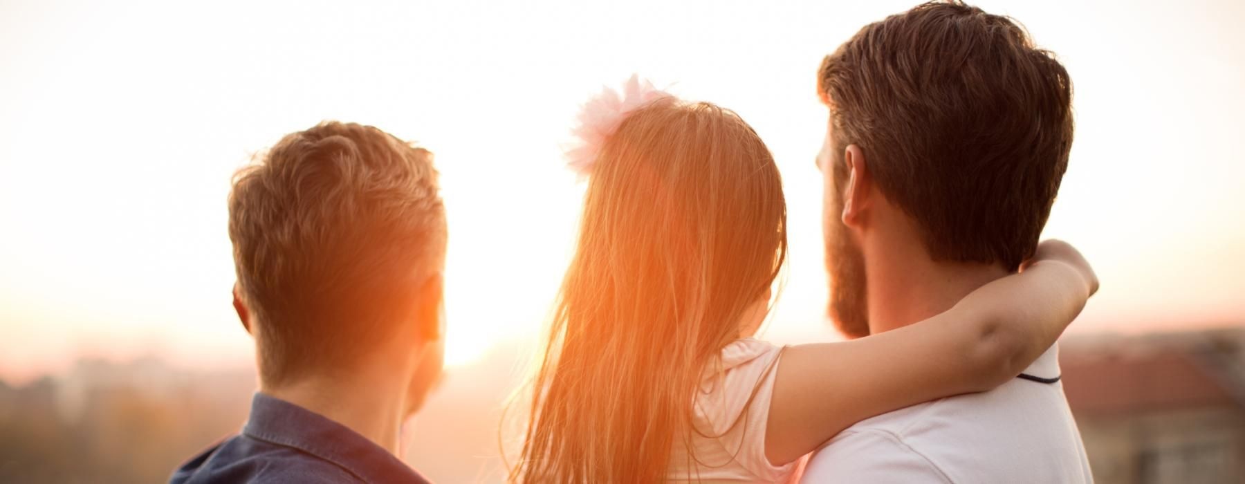 two men holding a little girl while looking at a sunset