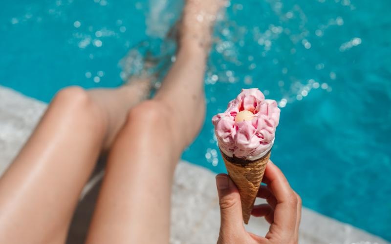 a person holding an ice cream cone while sitting out by the pool